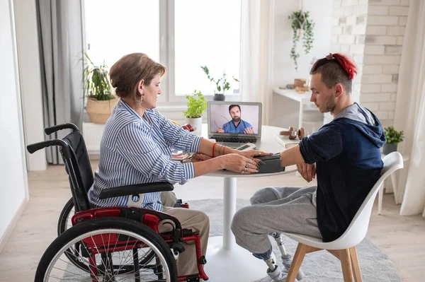 Disabled people sitting at the table indoors at home, video consultation with doctor. — Stock Photo, Image