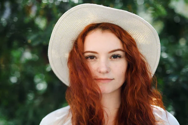 Close-up portrait of young woman with a hat outdoors in city, looking at camera. — Photo