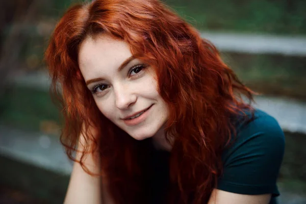 Portrait of young woman sitting outdoors on staircase in city, looking at camera. — Photo