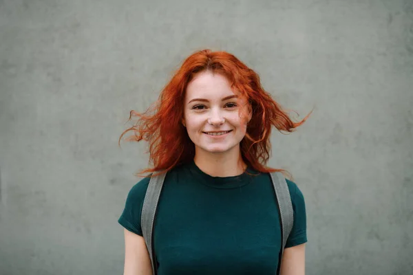 Portrait of young woman standing outdoors against gray background, looking at camera. — ストック写真