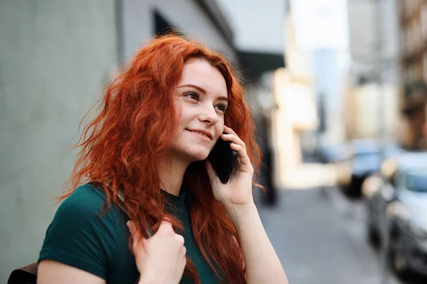 Portrait of young woman with backpack standing outdoors on city street, using smartphone. — Photo