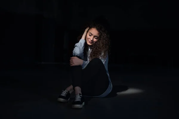 Portrait of happy young woman sitting indoors against black bacground. — Stock Photo, Image