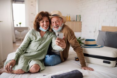 Senior couple taking selfie in hotel room, coronavirus, holiday and new normal concept.