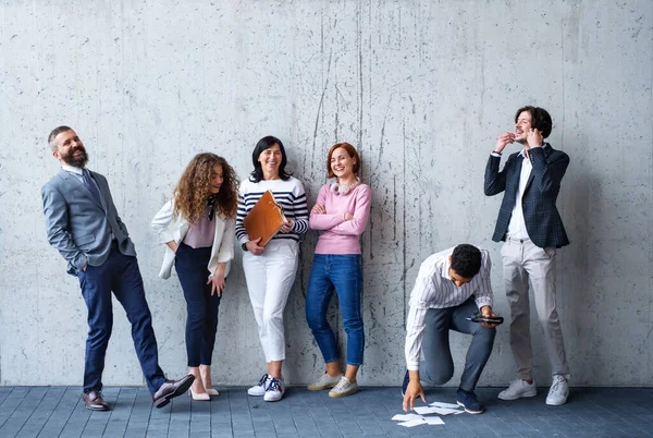 Portret van een groep ondernemers die binnen op kantoor tegen een betonnen muur staan te lachen. — Stockfoto