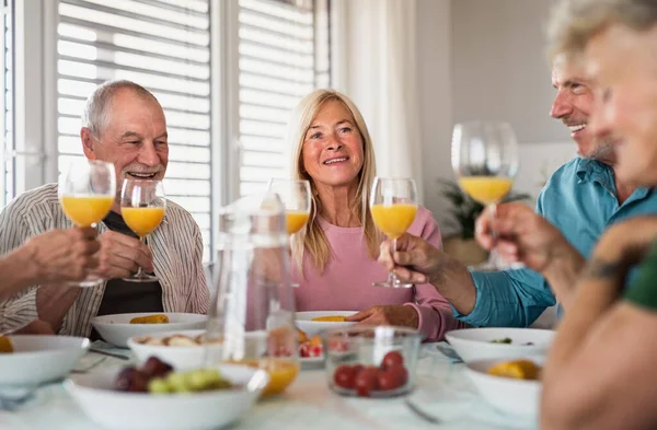 Gruppe älterer Freunde feiert drinnen, spricht beim Essen am Tisch. — Stockfoto