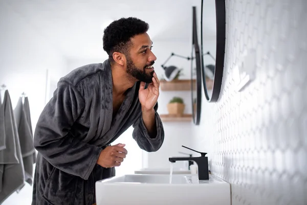 Young man washing face indoors at home, morning or evening routine concept. — Stock Photo, Image