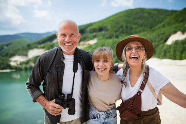 Felice ragazza preadolescente con i nonni in viaggio escursionistico in vacanza estiva, guardando la fotocamera. — Foto Stock
