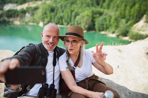 Ευτυχισμένο ζευγάρι ηλικιωμένων σε εκδρομή πεζοπορίας στις καλοκαιρινές διακοπές, κάνοντας γκριμάτσες όταν βγάζετε selfie. — Φωτογραφία Αρχείου