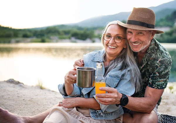 Casal sênior feliz em uma viagem de caminhada nas férias de verão, relaxando junto ao lago. — Fotografia de Stock