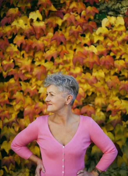 Mulher sênior em pé ao ar livre contra fundo outono natural colorido, descansando. — Fotografia de Stock