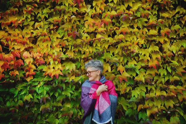 Ηλικιωμένη γυναίκα στέκεται σε εξωτερικούς χώρους κατά πολύχρωμο φυσικό φόντο φθινόπωρο. — Φωτογραφία Αρχείου