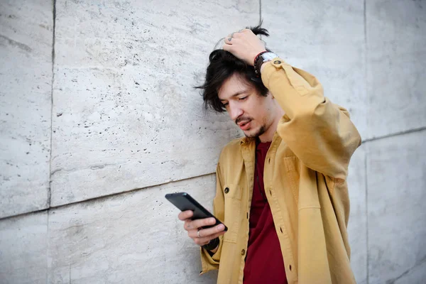 Retrato de un joven parado contra una pared de hormigón al aire libre, usando un smartphone. —  Fotos de Stock