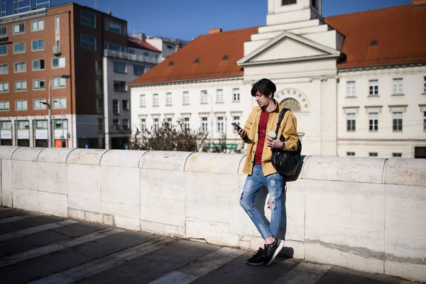 Portret van een jongeman die buiten in de stad staat, met smartphone. — Stockfoto