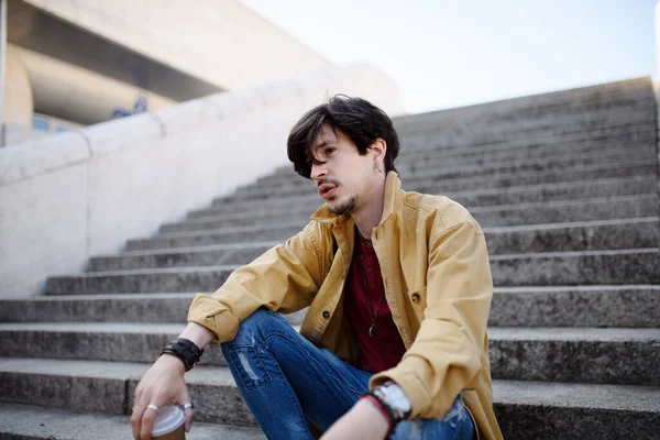 Портрет грустного молодого человека, сидящего на лестнице на открытом воздухе в городе, отдыхающего. — стоковое фото