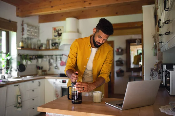 Jeune homme avec ordinateur portable et café travaillant à l'intérieur, concept de bureau à domicile. — Photo