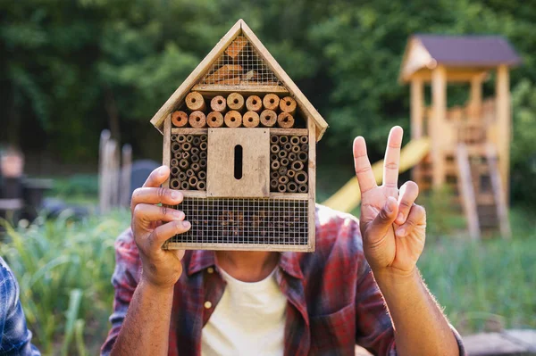 Happy young man with bug hotel spend time outdoors in backyard, showing v sign with fingers. — Stok Foto