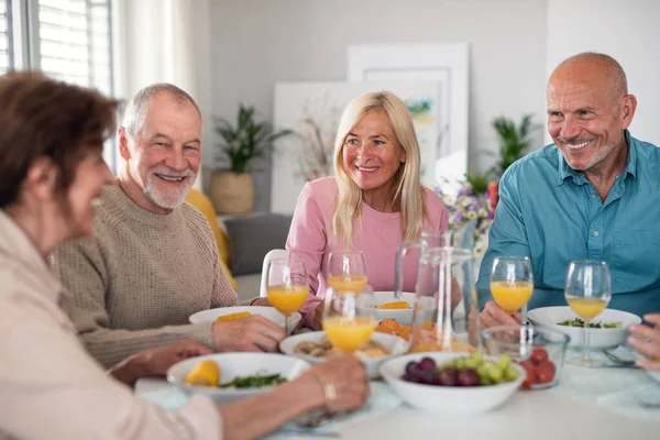 Gruppo di amici anziani che danno festa in casa, parlando quando si mangia a tavola. — Foto Stock