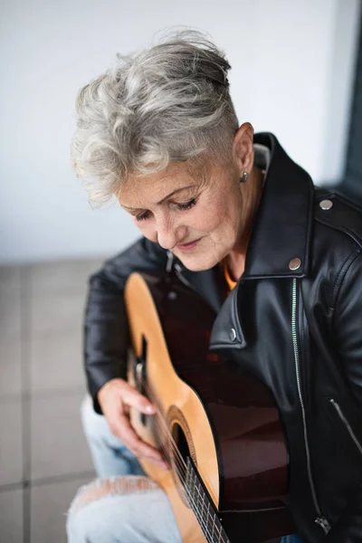 Portret van oudere vrouw zittend tegen zwarte achtergrond, gitaar spelend. — Stockfoto