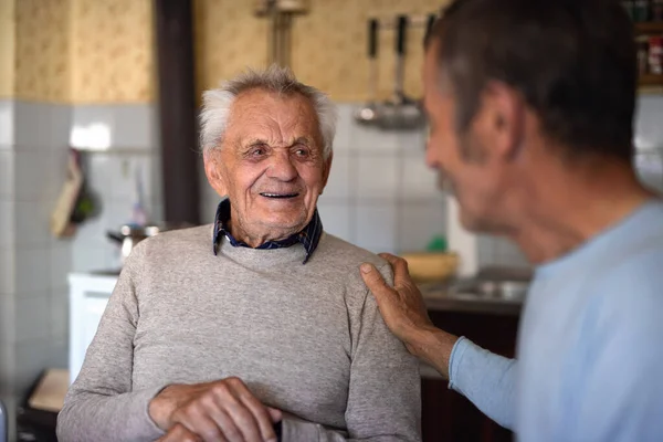 Portret van een man met een oudere vader die thuis aan tafel zit, pratend. — Stockfoto