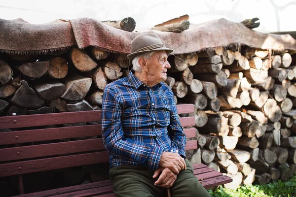 Porträt eines älteren Mannes, der im Garten auf einer Bank sitzt und sich ausruht. — Stockfoto