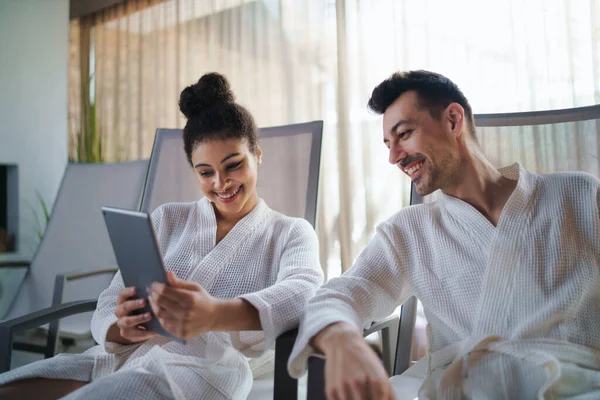 Portret van jong koppel ontspannen in kuuroord, met behulp van tablet. — Stockfoto