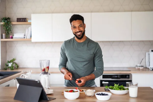 Junger Mann mit Tablet bereitet zu Hause gesundes Frühstück zu, Home-Office-Konzept. — Stockfoto