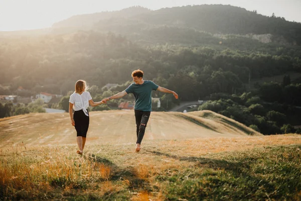 Young couple walking in nature at sunset in countryside, holding hands. — Stock Photo, Image