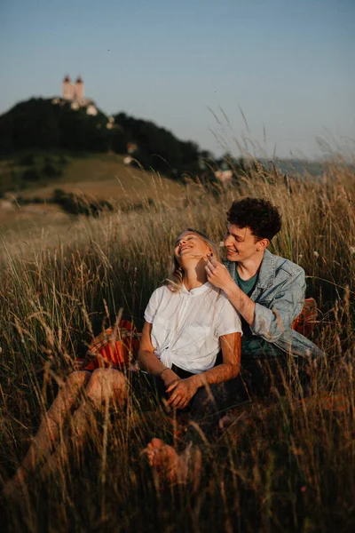 Young couple on a walk in nature at dusk in countryside, sitting and resting in long grass. — Stock Photo, Image