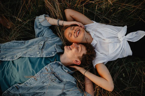 Draufsicht auf ein junges Paar bei einem Spaziergang in der Natur in der Landschaft, lachend im Gras liegend. — Stockfoto