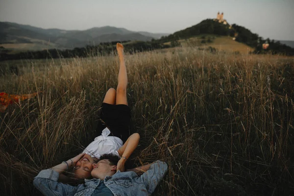 Jong stel op een wandeling in de natuur op het platteland, liggend in gras lachen. — Stockfoto