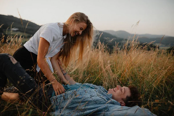 Young couple on a walk in nature in countryside, lying in grass laughing. — Stock Photo, Image