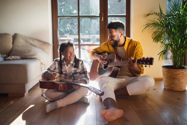 Evde gitar çalan küçük bir kızı olan mutlu bir babanın ön görüntüsü..