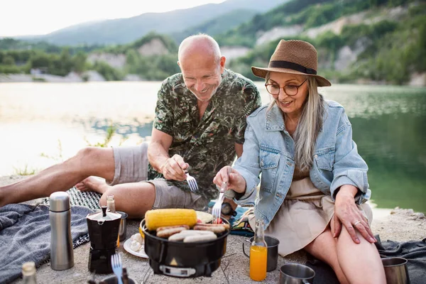 快乐的老夫妇在暑假旅行中休息，在湖边烧烤. — 图库照片