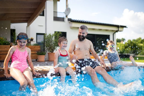 Padre con tres hijas al aire libre en el patio trasero, sentado junto a la piscina. — Foto de Stock