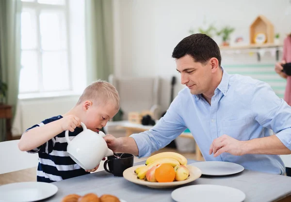 Família feliz com síndrome de down filho na mesa, tomando café da manhã. — Fotografia de Stock