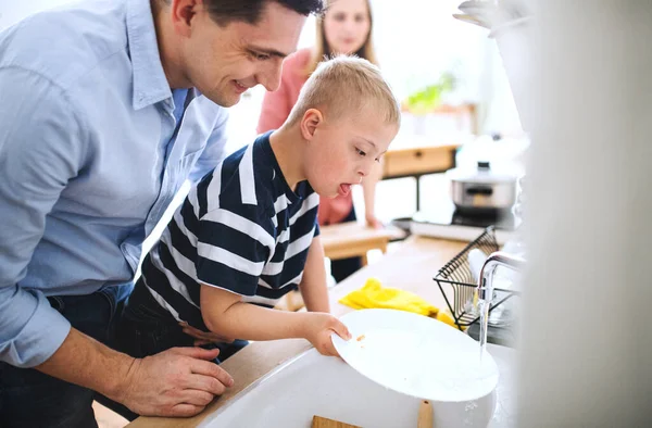 Vater mit Down-Syndrom-Sohn drinnen in Küche, spült Geschirr. — Stockfoto