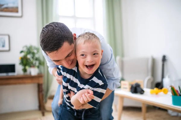 Pai com feliz síndrome de down filho dentro de casa, se divertindo. — Fotografia de Stock