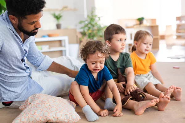 Mann tröstet weinenden kleinen Jungen im Kindergarten im Klassenzimmer. — Stockfoto