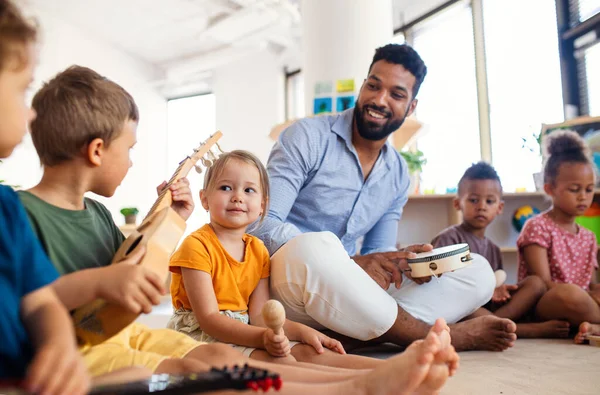 Gruppe kleiner Kindergartenkinder mit einem männlichen Lehrer, der im Klassenzimmer auf dem Boden sitzt und spielt. — Stockfoto