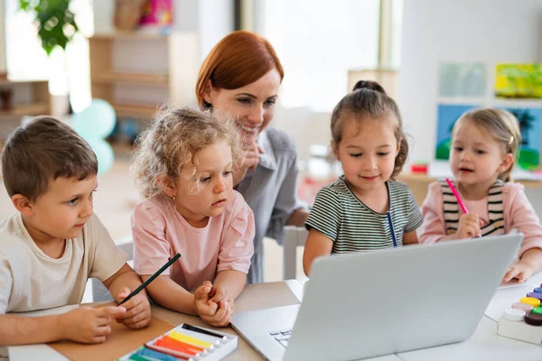 Groep kleine kleuterschoolkinderen met leraar op de vloer in de klas, met behulp van laptop. — Stockfoto