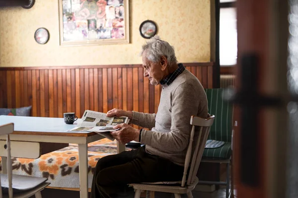 Retrato de homem idoso sentado à mesa dentro de casa, lendo jornais. — Fotografia de Stock