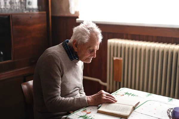 Porträt eines älteren Mannes, der zu Hause am Tisch sitzt und Buch liest. — Stockfoto