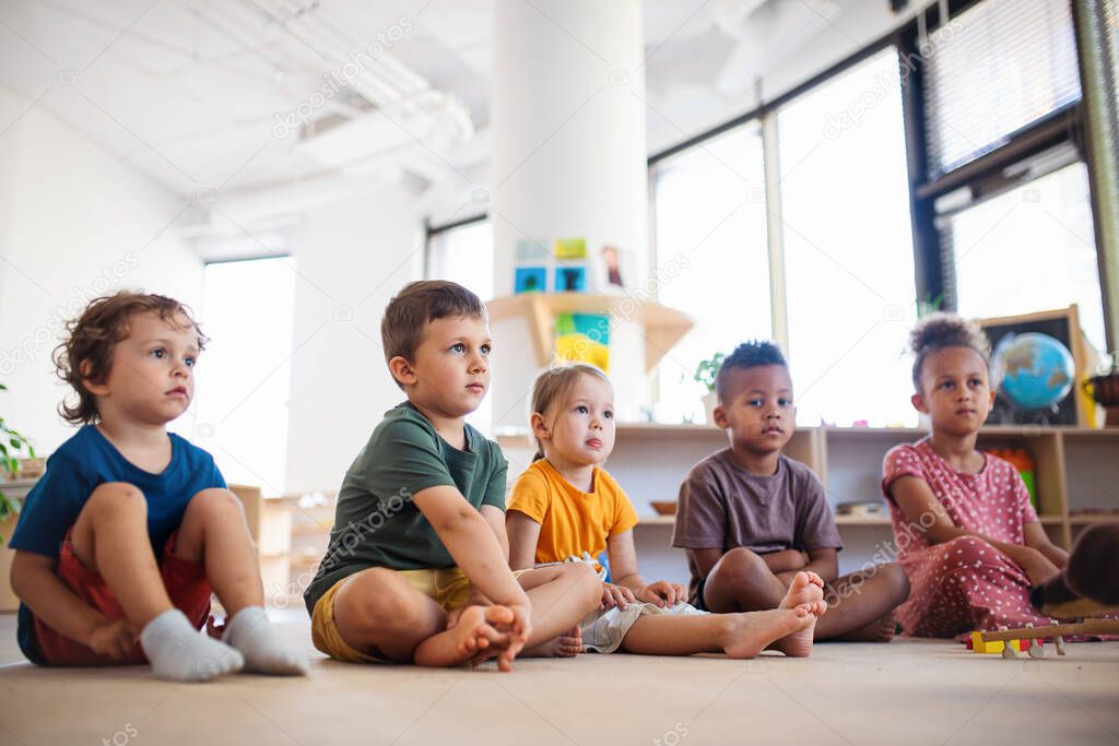 Group of small nursery school children sitting on floor indoors in classroom.