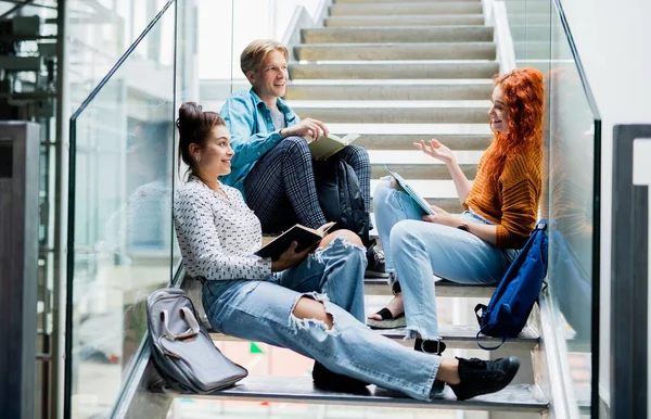 Universitetsstudenter sitter på trappor och pratar inomhus, tillbaka till skolkonceptet. — Stockfoto