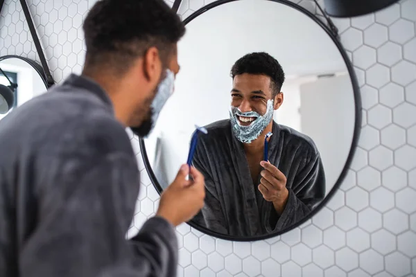 Hombre joven que usa barba de afeitar en el interior del hogar, concepto de rutina matutina o nocturna. — Foto de Stock