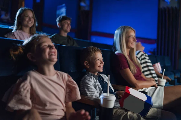 Moeder met gelukkige kleine kinderen in de bioscoop, kijken naar film en lachen. — Stockfoto