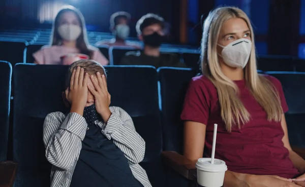 Menino assustado com a mãe cobrindo os olhos no cinema, assistindo filmes e conceito de coronavírus. — Fotografia de Stock