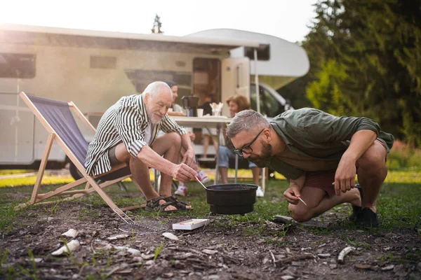 Mature man with senior father preparing barbecue at campsite outdoors, caravan family holiday trip. — Stock Photo, Image