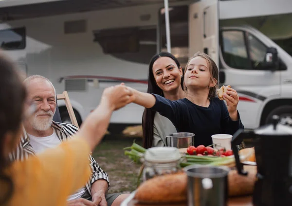 Flergenerationsfamilj som sitter och äter utomhus med bil, husvagn och semesterresa. — Stockfoto