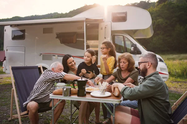 Multi-generation family sitting and eating outdoors by car, caravan holiday trip. — Stock Photo, Image
